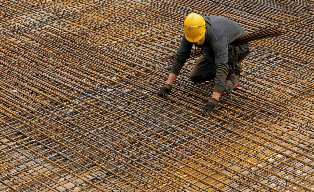 Công nhân cúi buộc thép trên một lưới thép sàn rộng